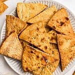 Crispy golden chips on a white plate in front of an air fryer.