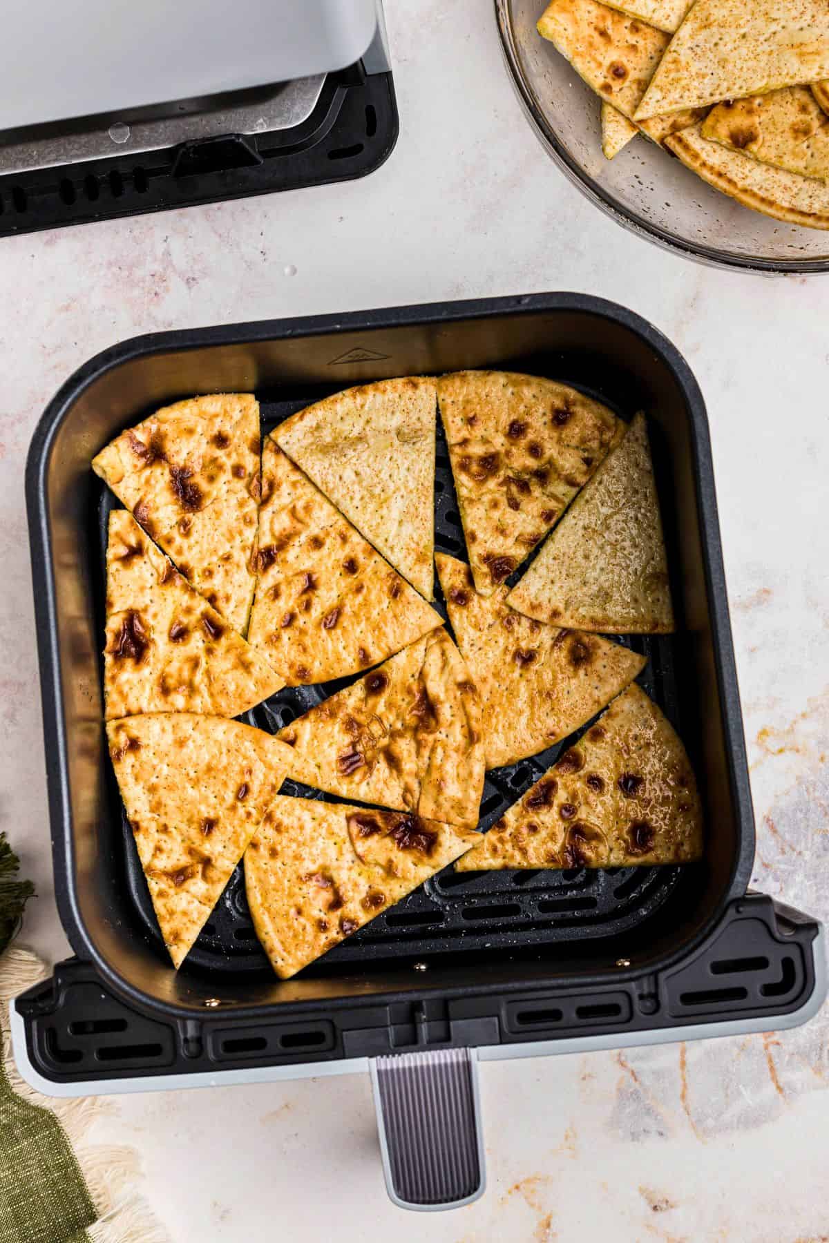 Pieces of pita bread in the air fryer basket before being cooked into chips. 