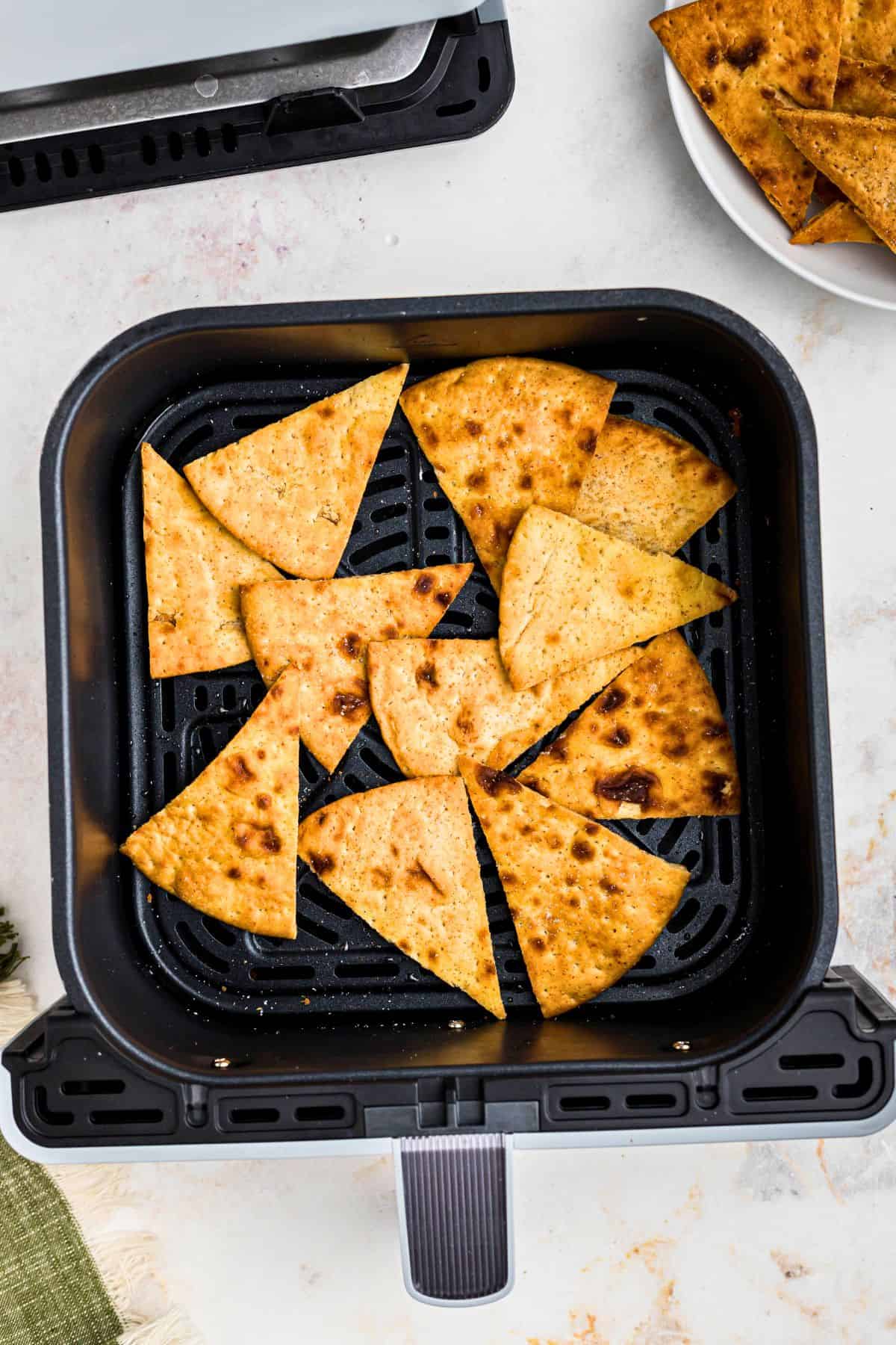 Crispy golden brown pita chips in the air fryer basket after being cooked. 