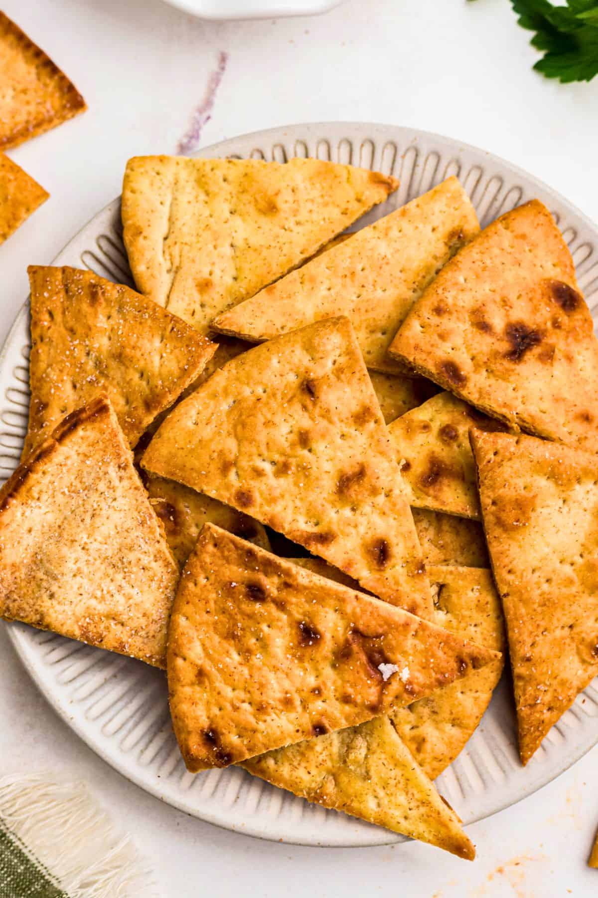 Crispy golden chips on a white plate in front of an air fryer. 