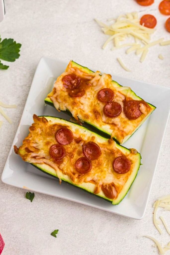 Zucchini boat pizza cut in half on a small white square plate. 