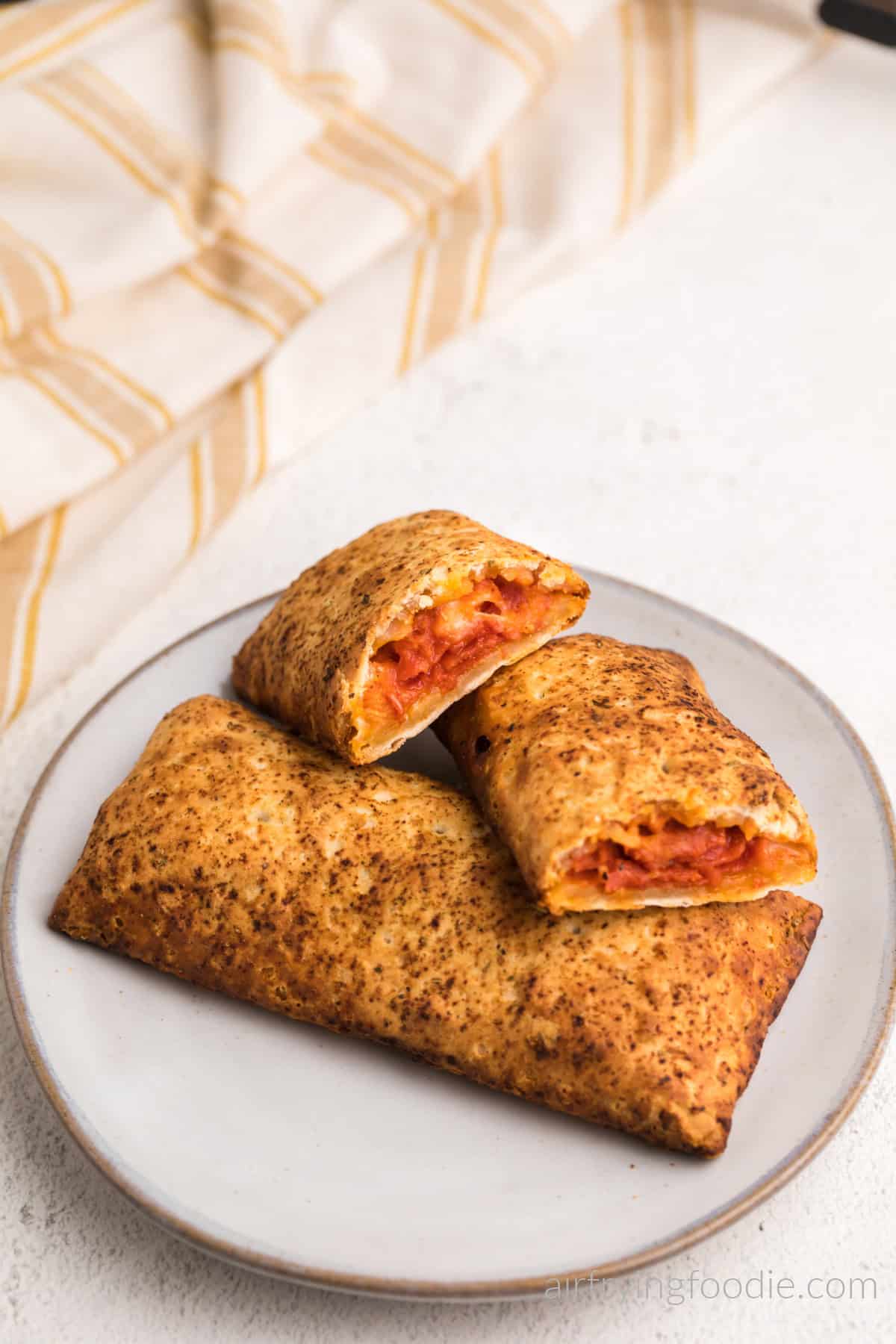 Air fried Hot pockets on a plate with one hot pocket cut in half, ready to eat. 