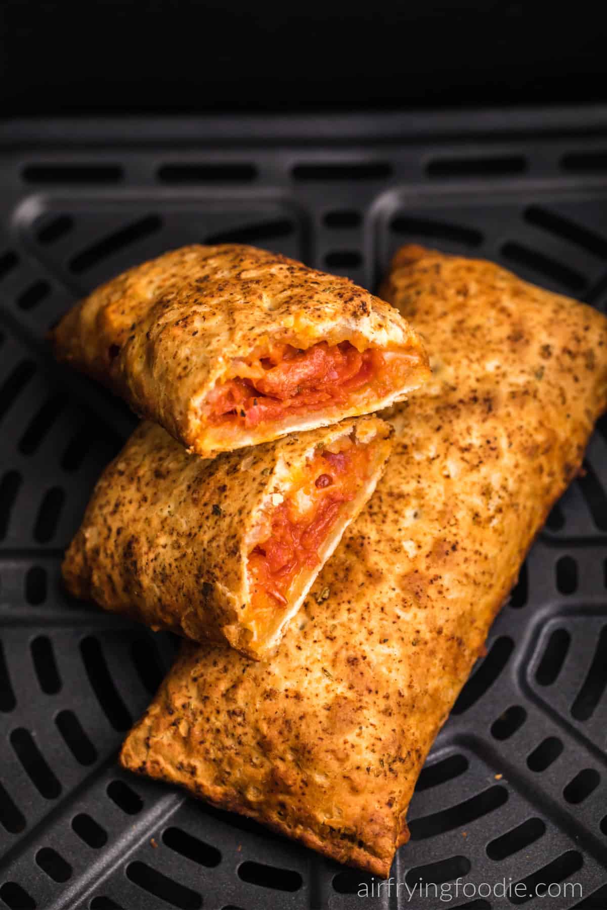 Hot pockets in air fryer basket, with one cut in half and ready to serve.