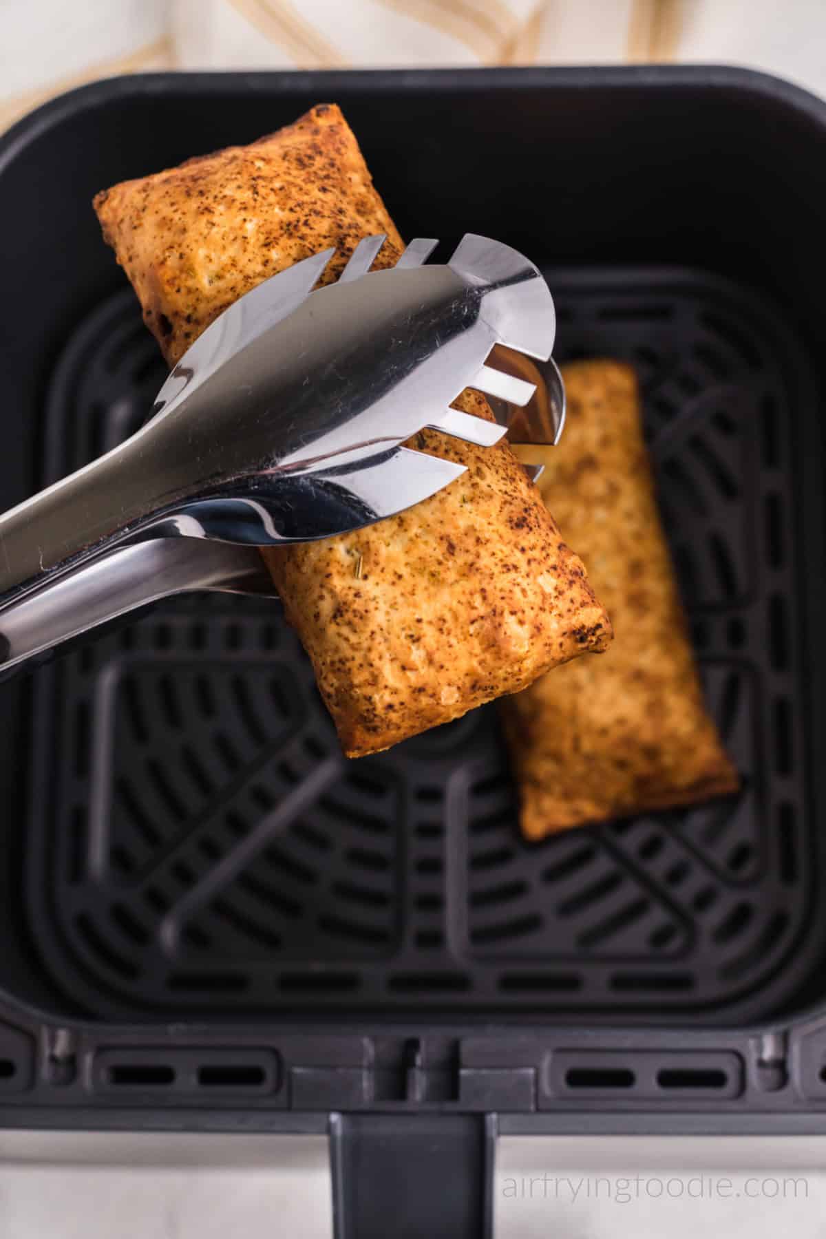 Hot pocket in air fryer basket and hot pocket in tongs over the air fryer basket. Ready to serve