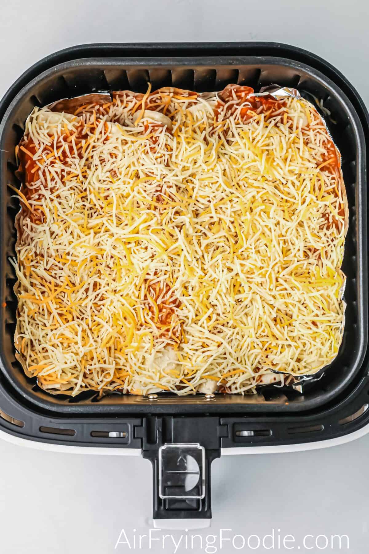 Enchiladas topped with cheese and sauce in the air fryer basket. 