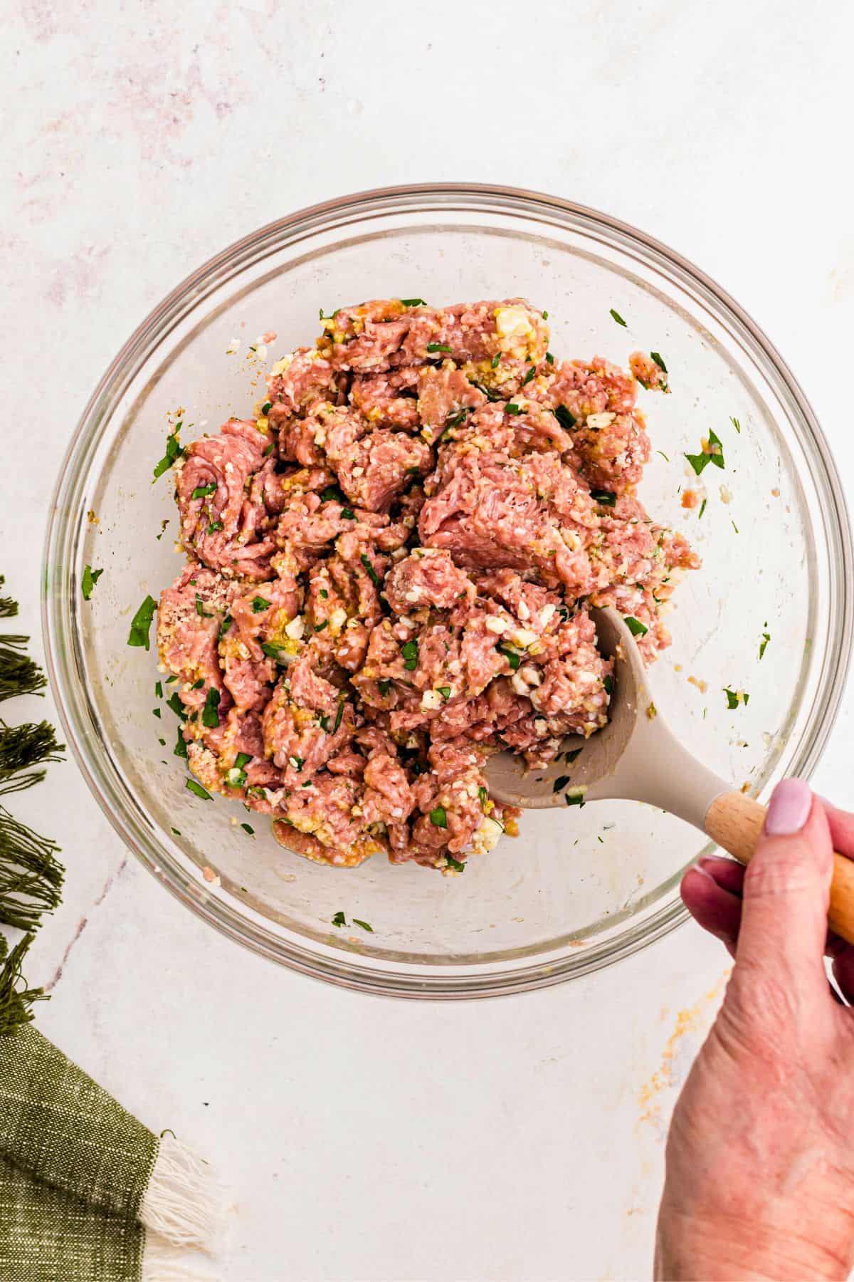 Ground turkey mixed in a large glass bowl with seasonings and breadcrumbs. 