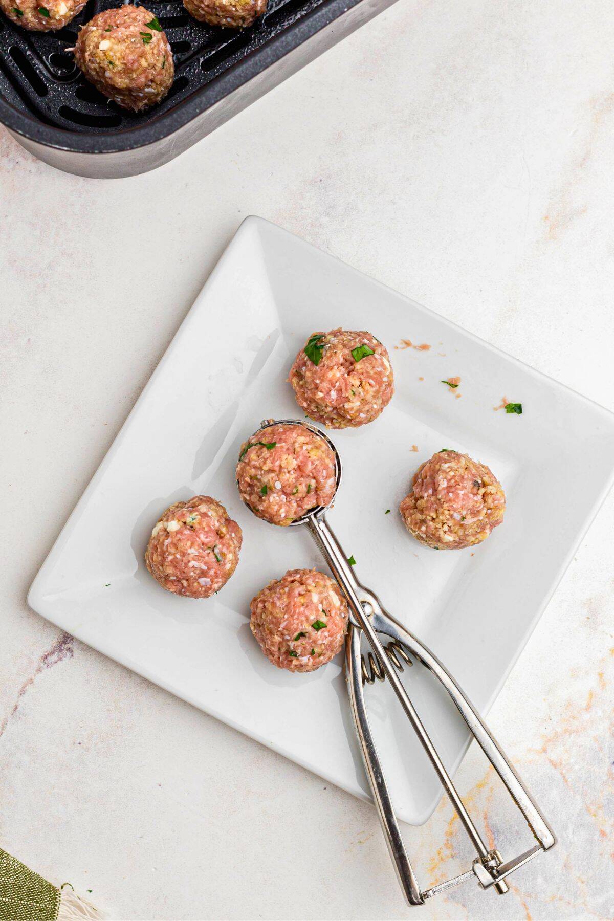 Greek meatball mixture scooped into small meatballs on a square white plate. 