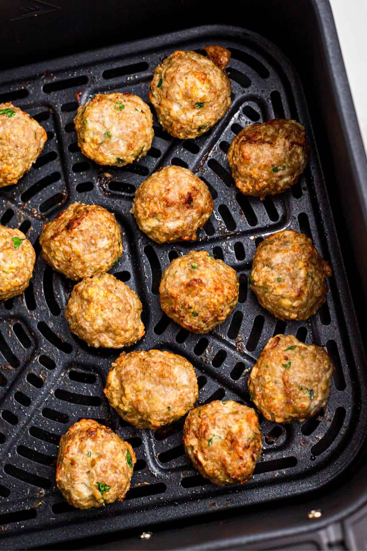 Juicy, golden Greek meatballs in the air fryer basket after being cooked. 