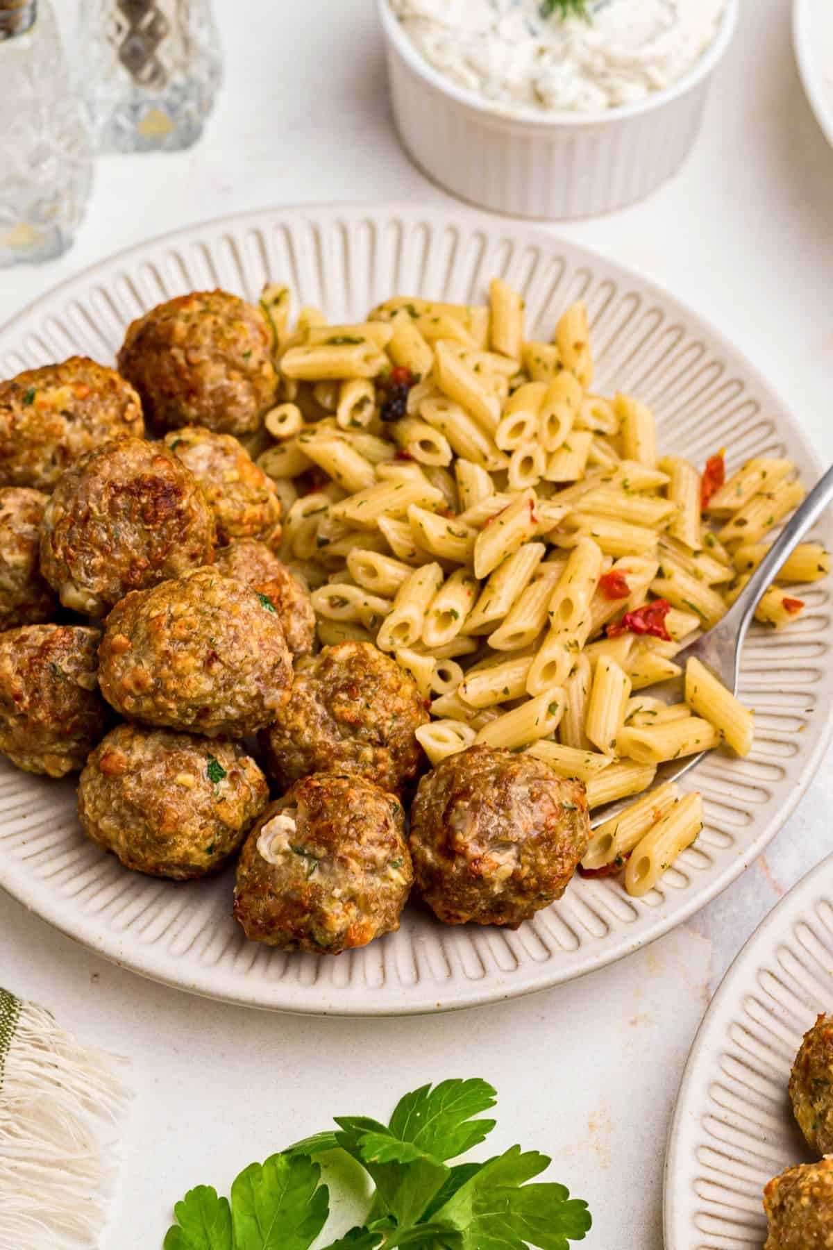 Juicy, golden Greek meatballs with pasta on a small white plate. 