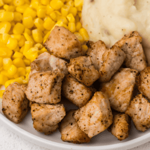 Close up of pork chop bites on a plate with corn and mashed potatoes.