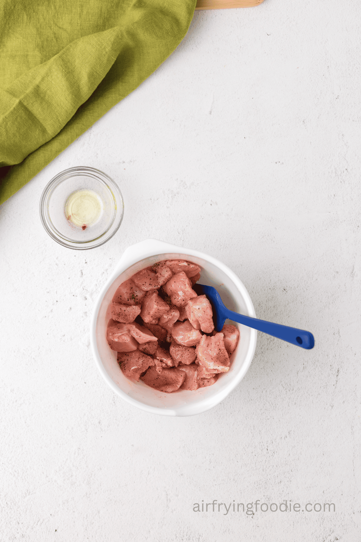Pork chop bites mixed together in a bowl with olive oil and seasonings. 