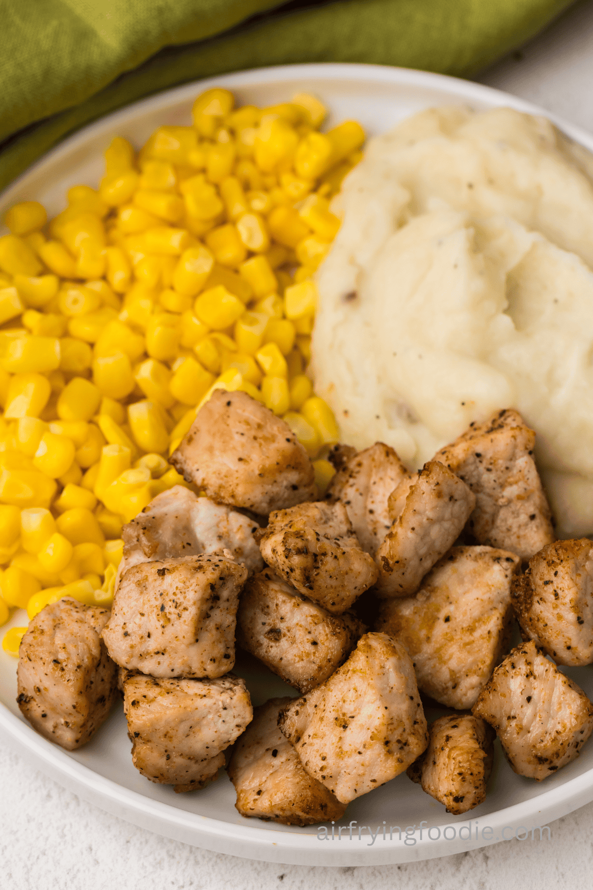 Close up of pork chop bites on a plate with corn and mashed potatoes.