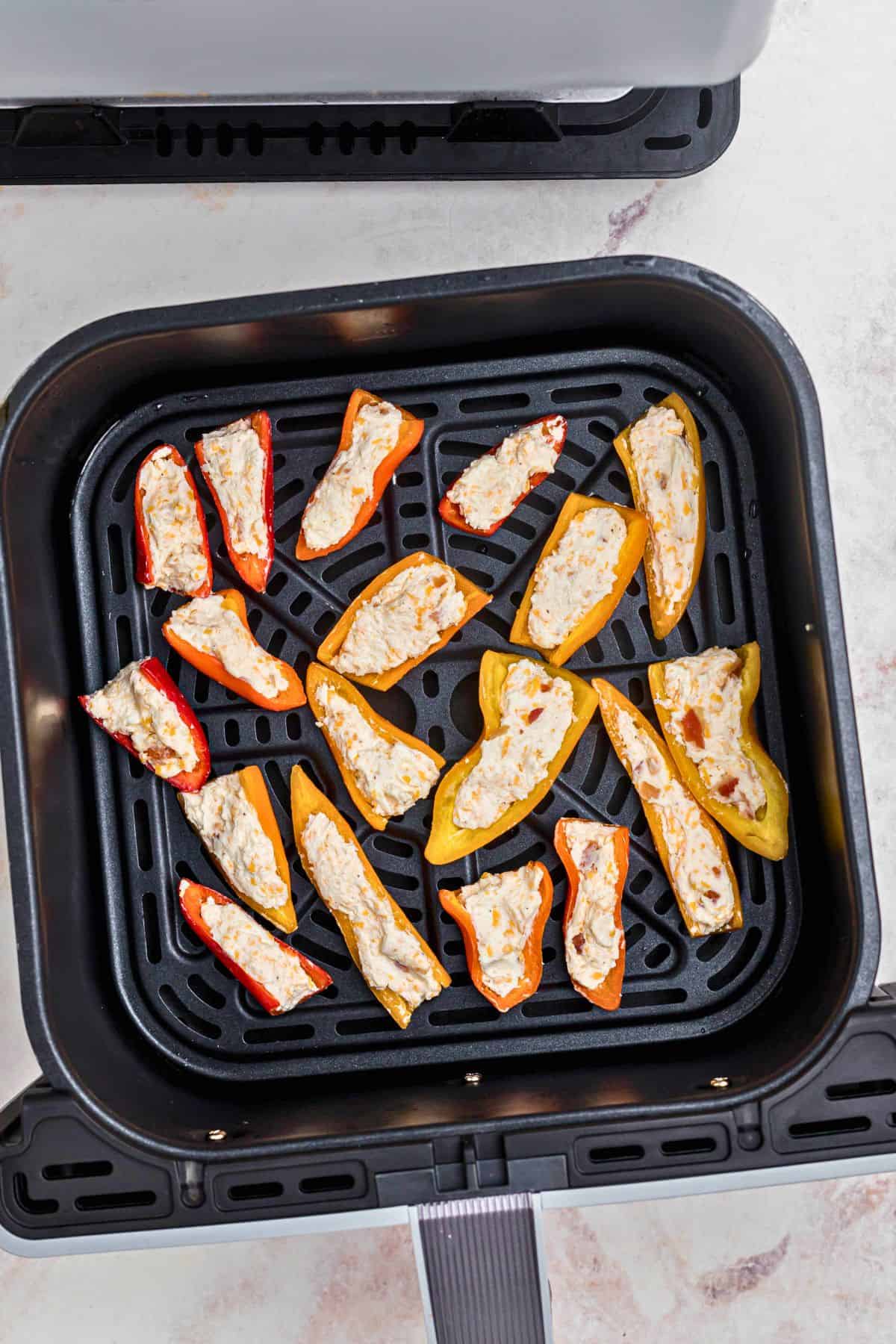 Mini peppers stuffed with cream cheese in the air fryer basket. 