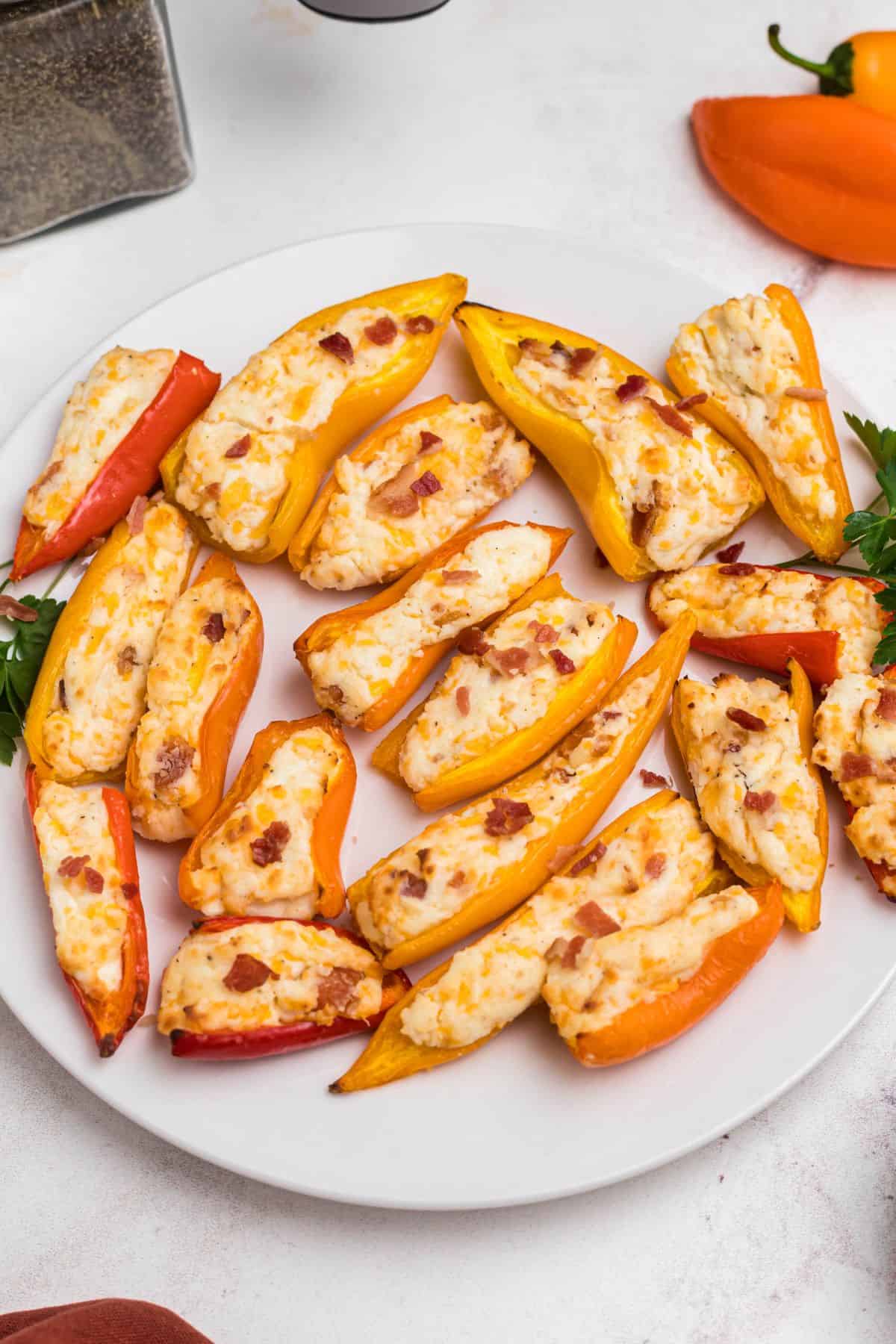 Red, orange, and yellow mini stuffed peppers on a white plate in front of an air fryer.