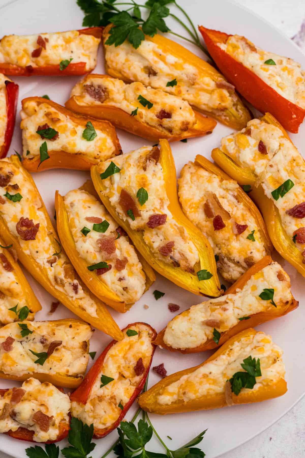 Red, orange, and yellow mini stuffed peppers on a white plate in front of an air fryer.
