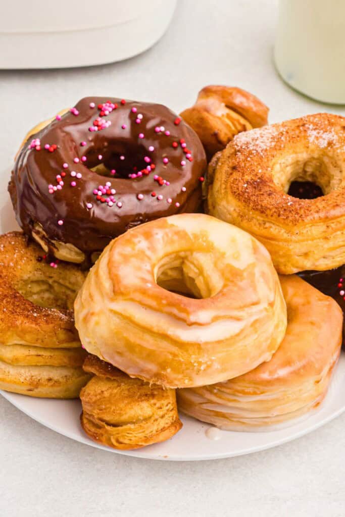 Plate of glazed, sugar coated, and chocolate covered golden donuts on a white plate served on a white marble table.