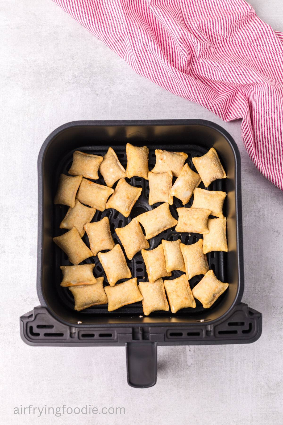 Uncooked pizza rolls arranged in an air fryer basket. 