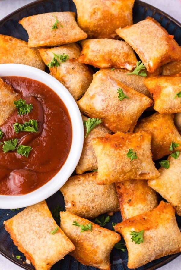 Air fryer pizza rolls on a plate with one dipped in tomato sauce.