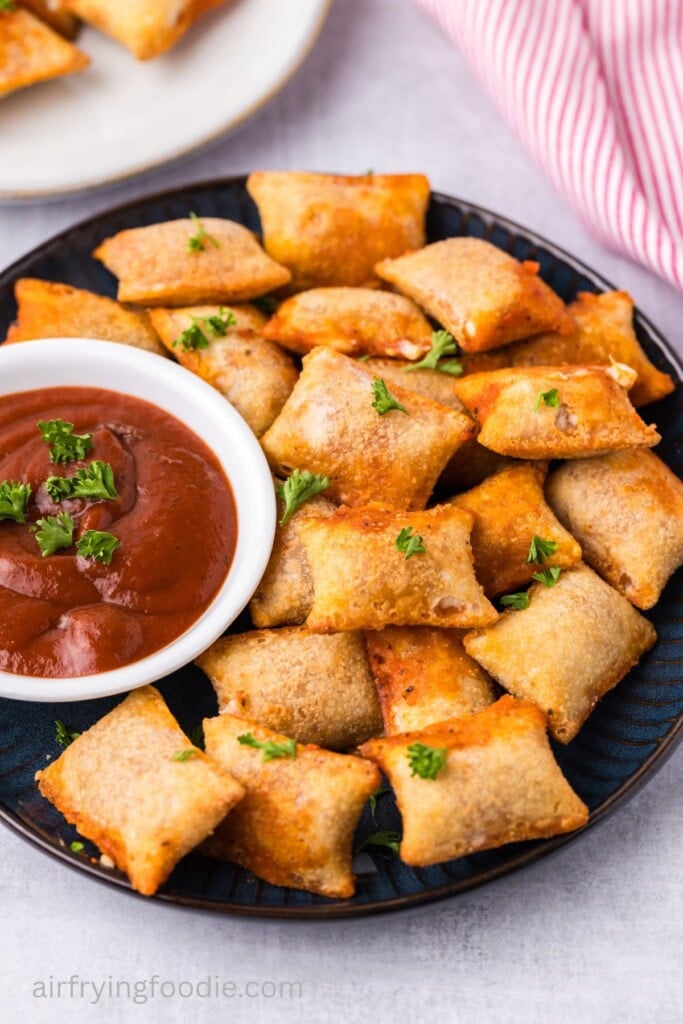 Air fryer pizza rolls on a black plate next to a bowl of marinara sauce. 