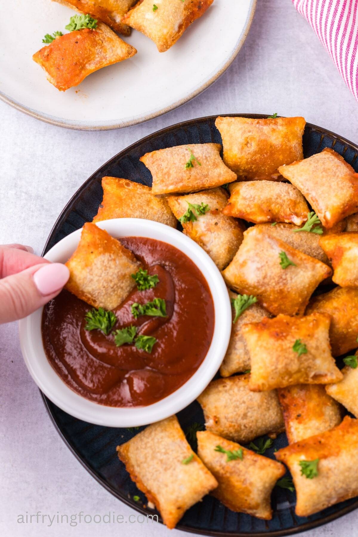 A hand reaching in to dip an air fried pizza roll in some marinara sauce. 
