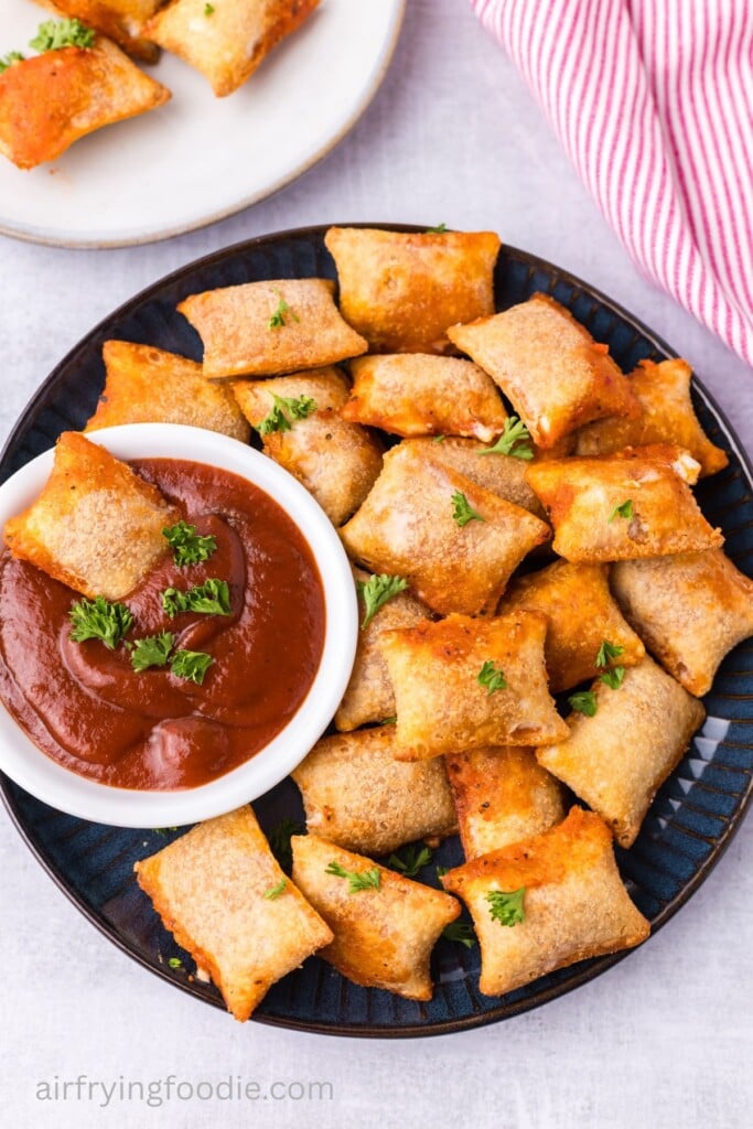 A plate of air fryer pizza rolls with a bowl of marinara sauce on the side.