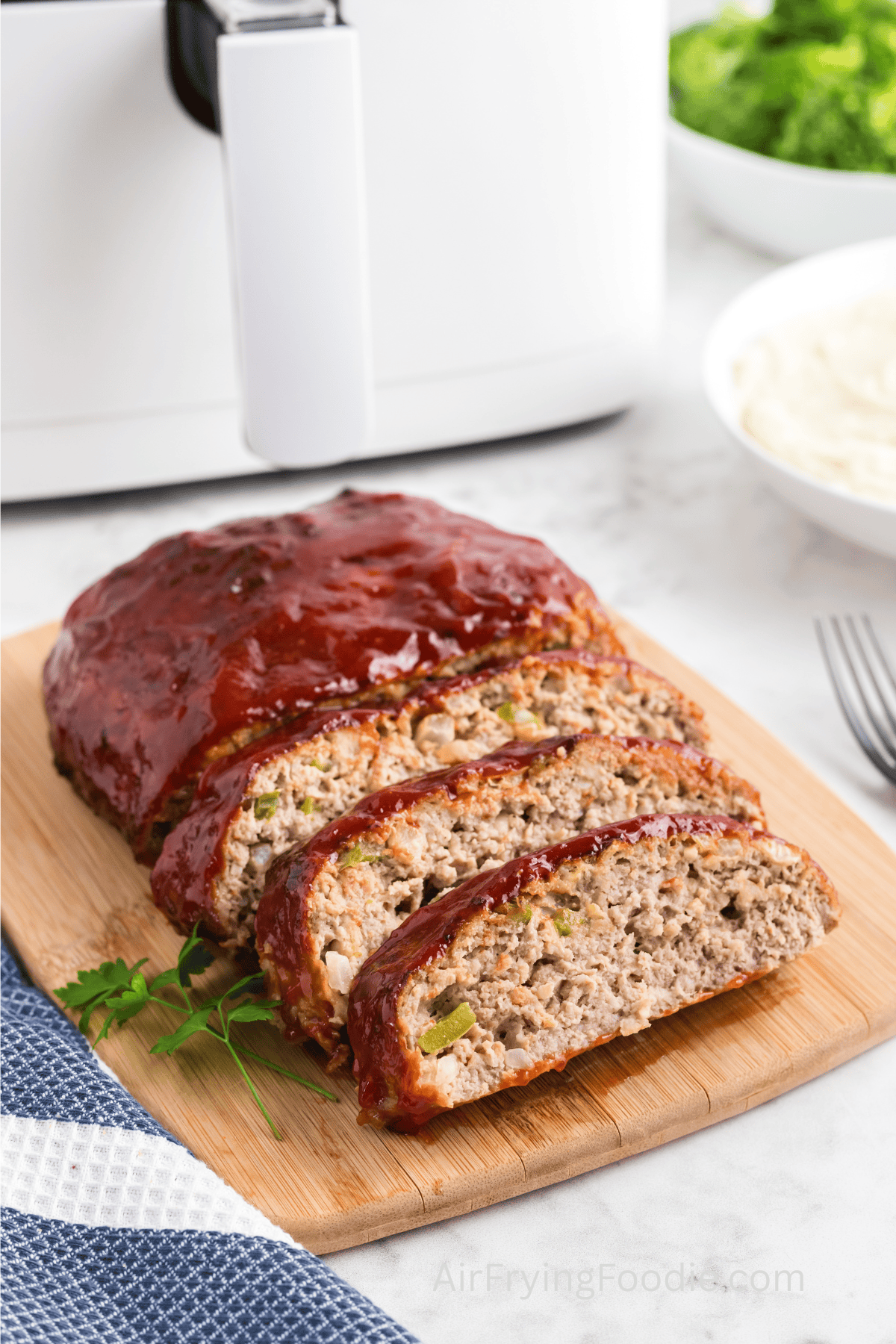 Turkey meatloaf air fried and sliced on a cutting board on a table in front of an air fryer.