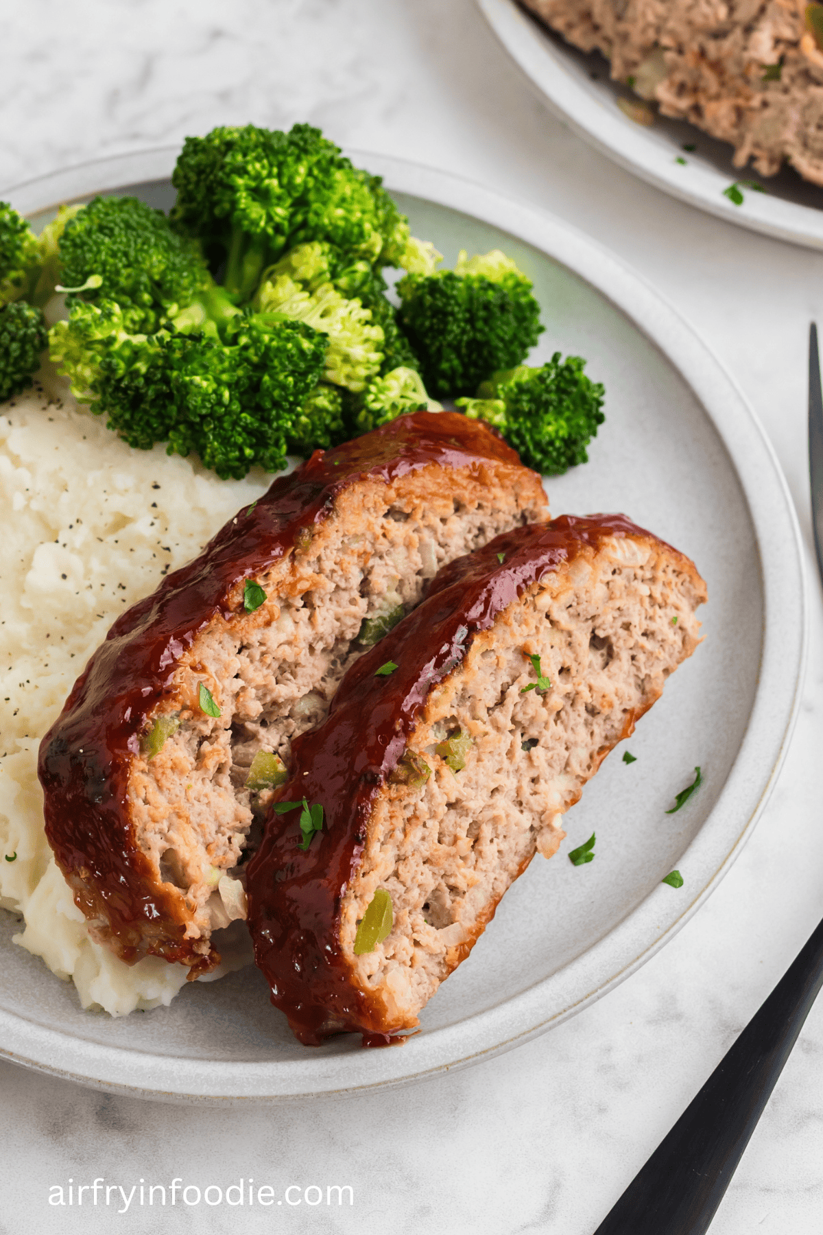 Sliced air frried turkey meatloaf on a plate with mashed potatoes and a side of broccoli.