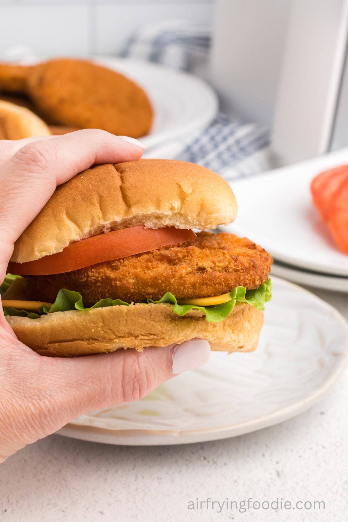 Tyson air fryer chicken patty on a bun with a hand picking it up from a plate.