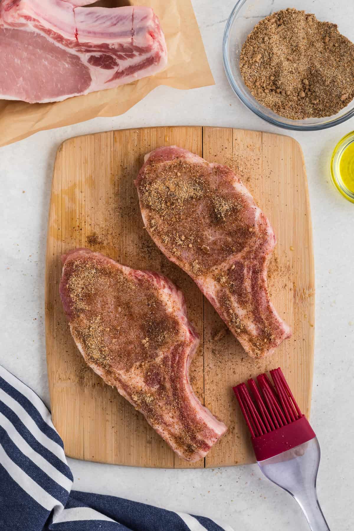 Pork steaks on a cutting board with seasoning added.