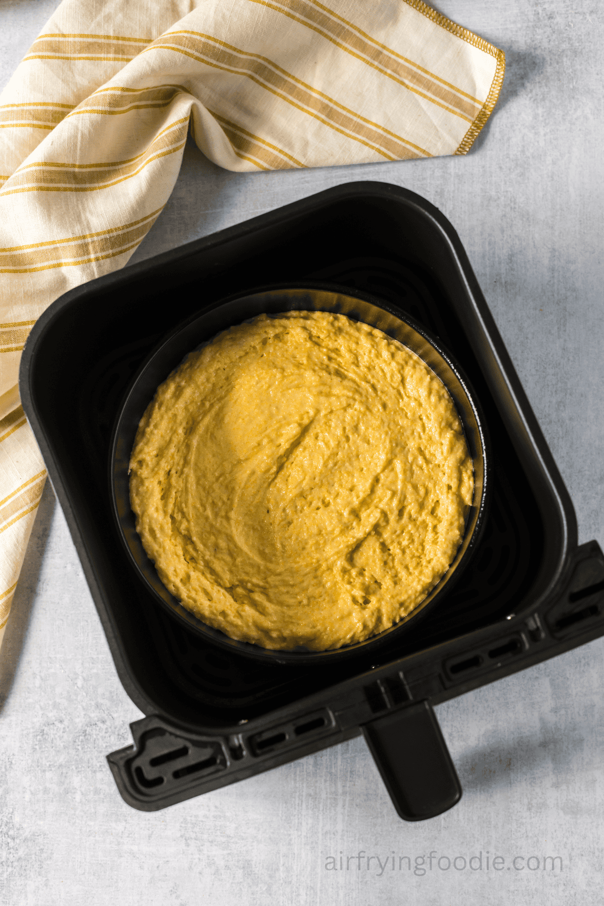 Cornbread batter added to a round pan and in the air fryer basket.