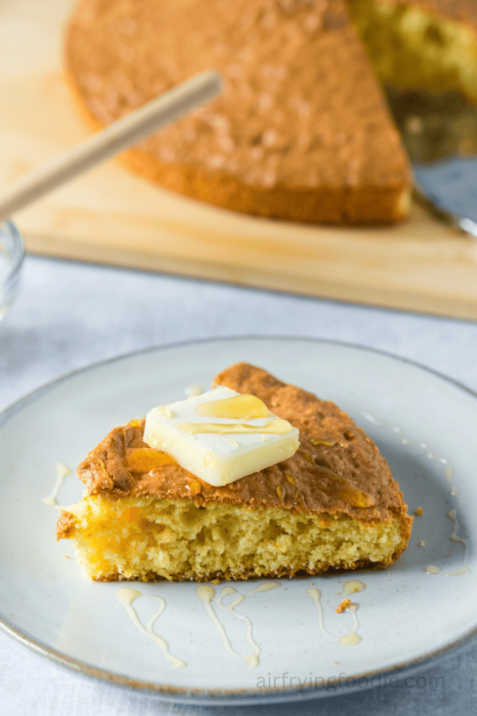 A slice of air fryer cornbread on a plate topped with a pat of butter. 