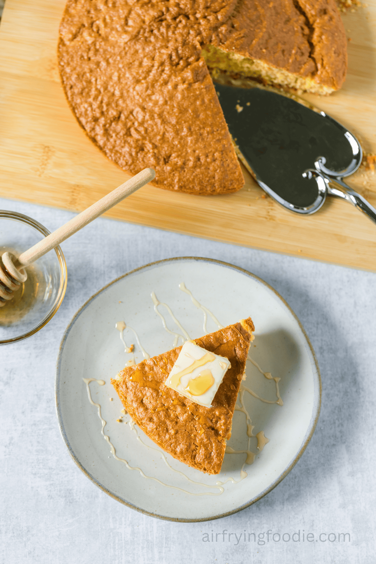 A slice of air fryer cornbread on a white plate topped with butter and the rest of the cornbread to the side.