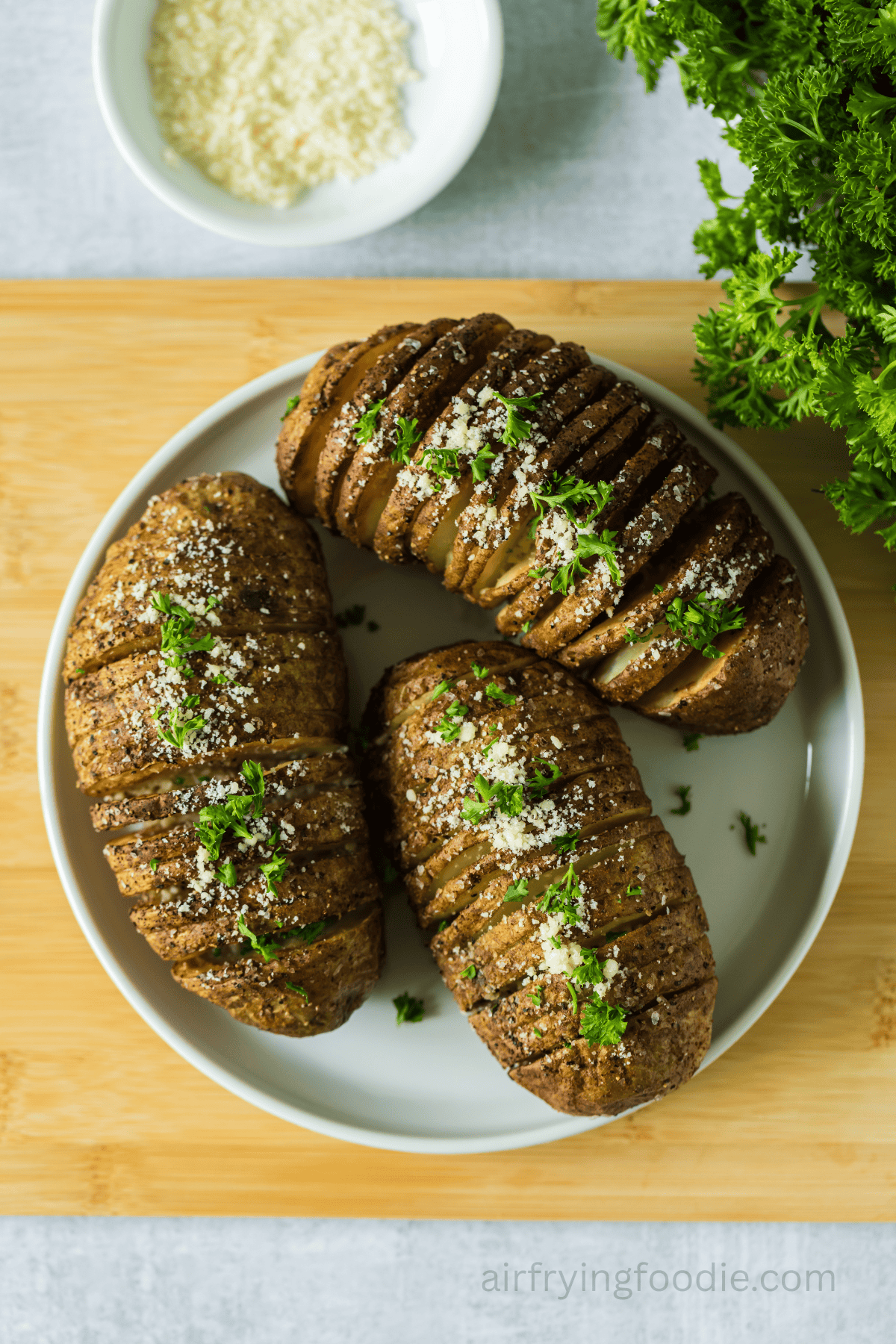 Air-fried Hasselback potatoes on a white plate with parsley on top.