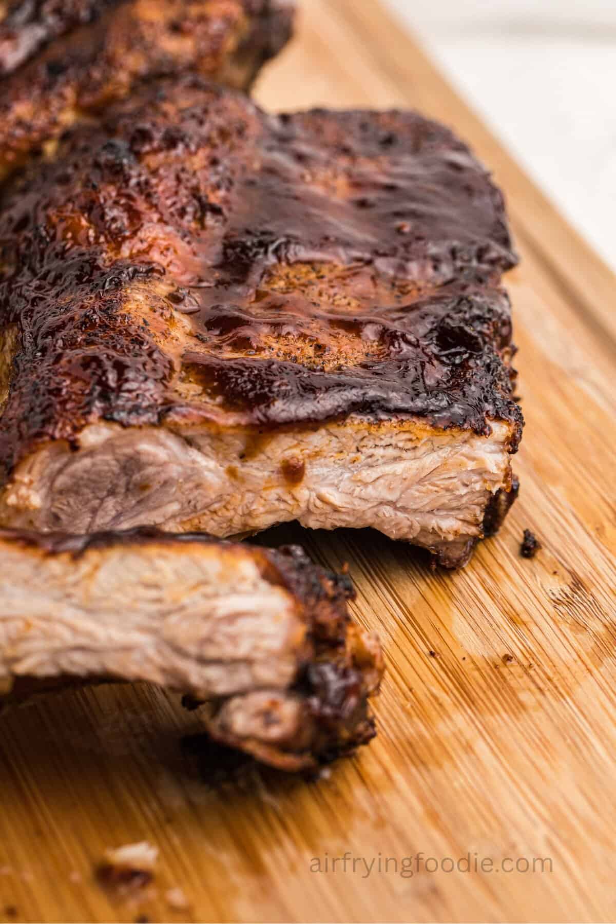 Air fryer ribs slathered in bbq sauce and sliced on a wooden cutting board.
