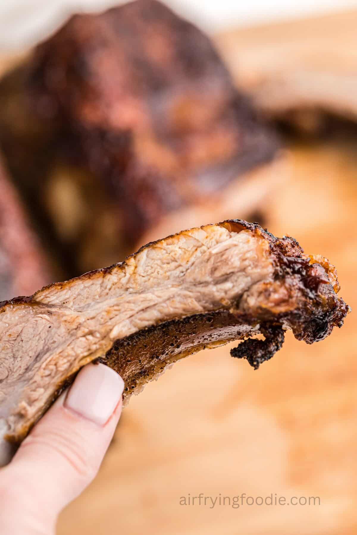 A hand holding up an air-fried BBQ rib.