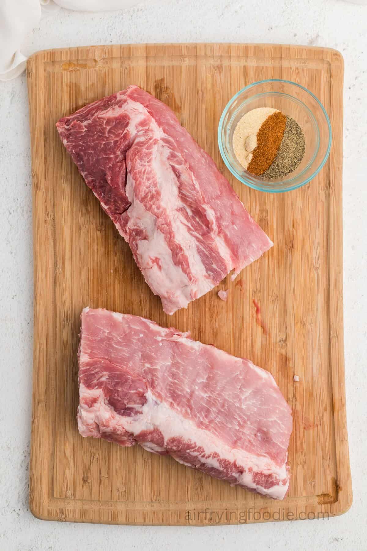 Ribs on a cutting board with seasonings in a small bowl.