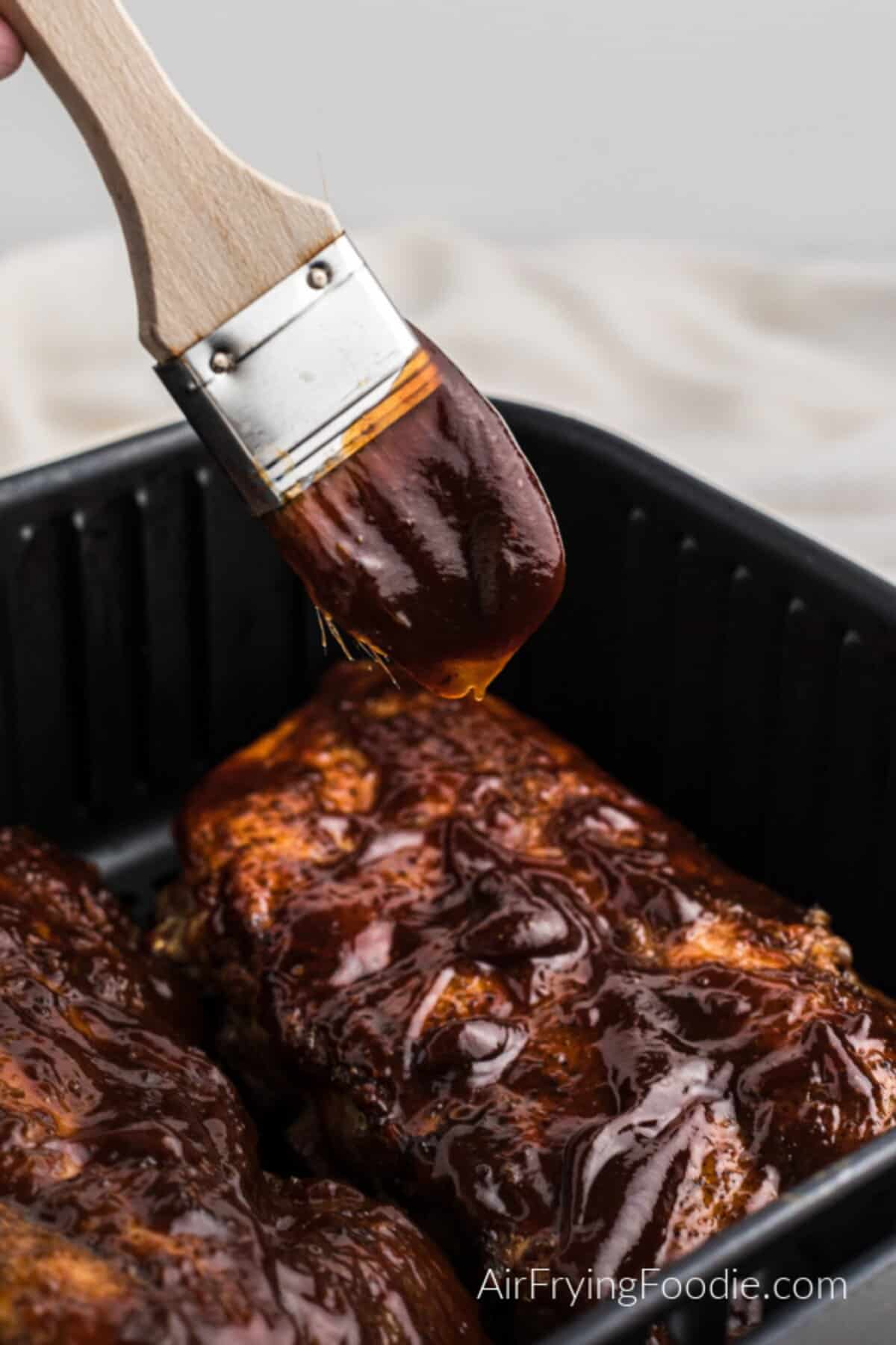 BBQ ribs in the air fryer basket with a brush adding some more sauce.