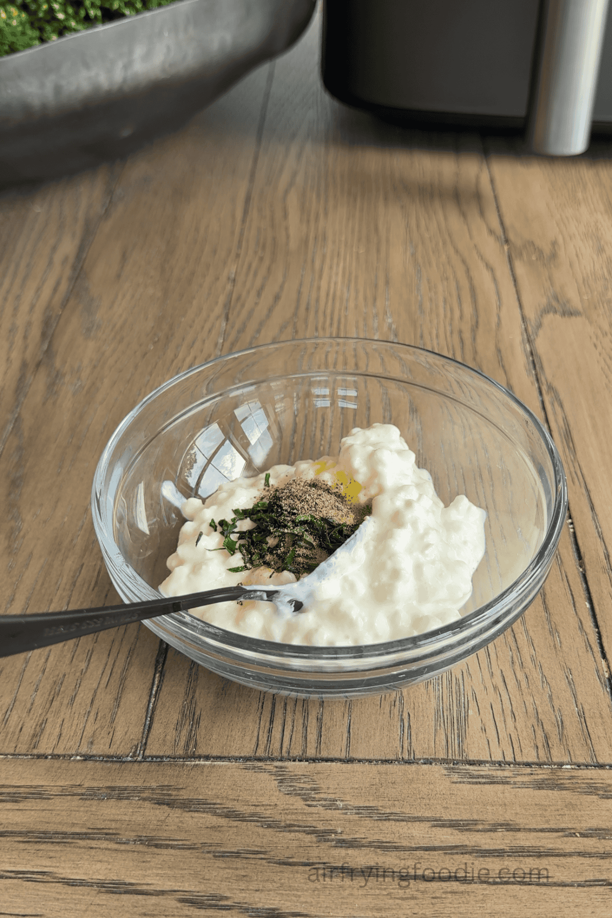 Herbs and seasonings being added to a bowl with cottage cheese.