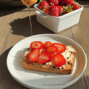 honey being drizzled over sliced strawberries on cottage cheese toast.