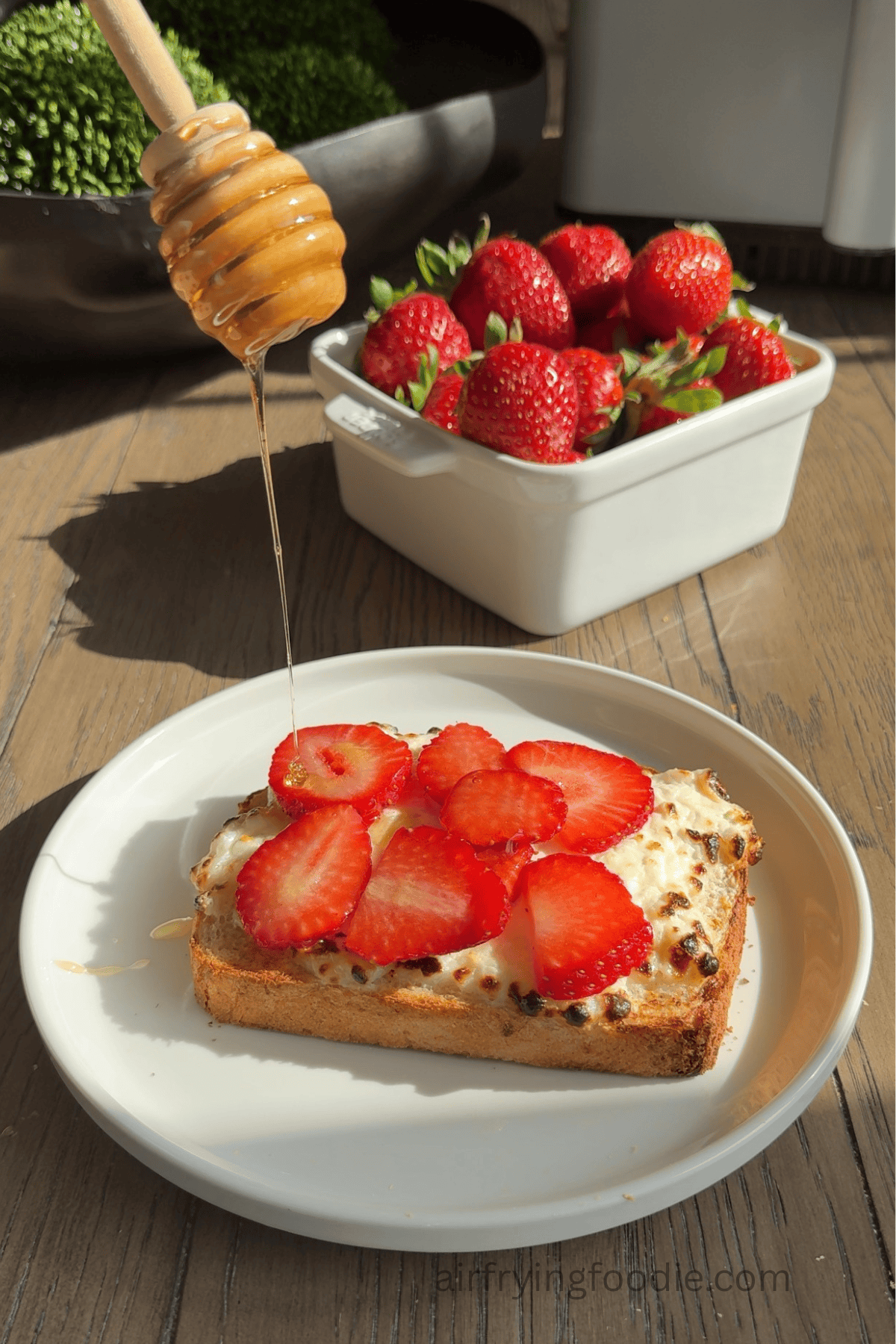Honey being drizzled over sliced strawberries on top of cottage cheese toast.