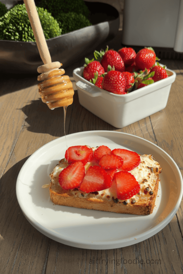 sliced strawberreis on cottage cheese toast, with honey being drizzled on top